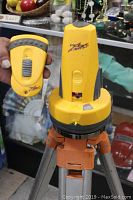 Close-up showing yellow Robo Laser rotary laser laser level with remote control held beside it; both display Robo Laser logo and are yellow with gray accents.