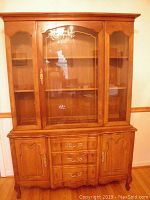 Front view of solid wood hutch showing glass doors, wooden lower cabinets and drawers, decorative hardware.