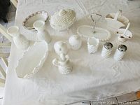 Full collection displayed on white cloth showing multiple hobnail milk glass pieces, candy dish with lid, salt and pepper shakers, cruet, votive holder, relish dish with handle and Royal China International bowls.