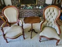 Front view of the two antique parlor chairs and Queen Anne end table in front of a brick fireplace.