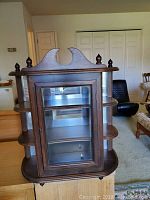 Curio cabinet front view showing glass door and decorative top with finials.