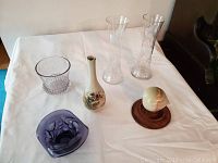 Photo of entire lot showing six items on table: two tall etched glass vases, large clear glass tumbler/vase with hobnail bottom, small Otagiri ceramic quail bud vase, purple Near Cut glass top hat vase, and a polished agate acorn on wooden pedestal.