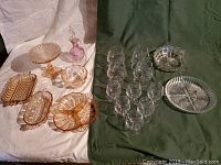 Photo showing a wide variety of glassware including clear brandy snifter glasses, clear aperitif glasses, pink glass candy and serving dishes, a pink and clear glass perfume bottle with stopper.