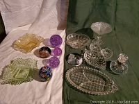 Photo showing assortment of glass dishes, paperweights, and perfume bottle arranged on white and green fabric background