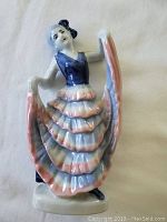 Close-up of a blue and pink pleated skirt lady figurine with raised arms holding out the skirt, dressed in detailed vintage clothing.