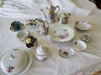 Group photo showing all items together including teapots, dessert dishes, vase, and decorative ceramic pieces on a white cloth background.
