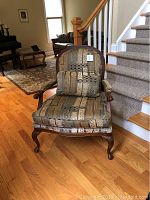 Full front view of upholstered armchair showcasing patterned fabric, mahogany legs, armrests, and cushioned seat with back pillow.