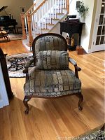 Full view of armchair with patterned upholstery and wood frame in home setting.