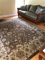 Full view of brown floral area rug on hardwood floor next to sofa