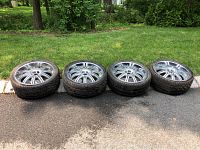 Four custom rims with tires aligned horizontally on pavement with grass background.