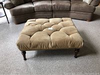 Full view of square tufted ottoman in tan microfiber with wooden legs and nailhead trim, showing overall design and condition.