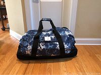 Front view of large floral blue print rolling duffel bag on hardwood floor.