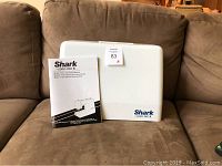 Sewing machine carrying case with instruction manual placed on a brown couch.