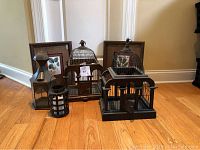 Two decorative birdcages, two lanterns (one metal, one plastic with battery-operated candle) grouped on wooden floor.