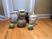 Full view of all seven assorted containers displayed on wood floor, showcasing variety in size, color, and style