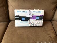 Two boxed SiriusXM Onyx satellite radios placed on a brown couch, showing front packaging with product images and branding.