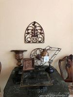Full view of lot items showing two metal wall hangings mounted on wall, wooden wall sconce and square wooden wall hanging on table, metal lamp on table.