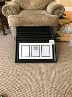 Seven stacked black wooden frames with triple 5x7 matted openings shown on carpet in front of armchair.