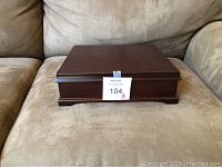 Closed cherrywood tea chest with dark polished wood finish sitting on a beige fabric couch