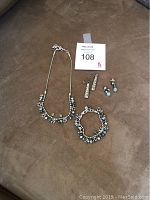 Photo of full Brighton jewelry set including necklace, matching bracelet, two sets of earrings arranged on brown surface.
