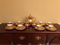 Full view of coffee pot, cups on saucers, arranged on a sideboard, showing gold finish and set composition.