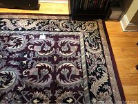 Full view of wool pile area rug on hardwood floor showing detailed floral and leaf design in burgundy and black.