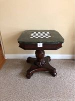 Full view of pedestal game table showing carved mahogany base and fossil stone veneer top with chessboard inlaid.
