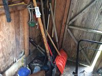 Various yard tools including shovels, snow shovels, a metal rake, hand tools, metal baseball bats, and a sprinkler, stored inside a wooden shed.