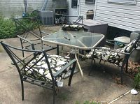 Patio table and four chairs with floral cushions arranged on concrete patio, visible rust on metal frames.