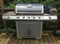 Full front view of grill on deck showing six control knobs, side shelves and cabinet doors