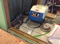 Photo of metal weight plates, dumbbells, and a blue and white Playmate 7 qt cooler on tiled floor.