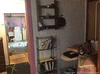 Photo showing the metal five-shelf stand with books and papers on shelves, wooden wall shelf mounted on wall with items hanging, surrounding area context