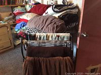 Photo showing multiple folded blankets, comforters, pillowcases, and throw pillows stacked on furniture and shelves.