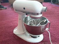 Front-left view of white mixer attached to bowl showing tilt-head and attachments inside bowl