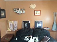Wall art and decor displayed on ochre wall including two metal sailboat sculptures, framed pictures, wooden oars, shelf with small ships, and mirror.