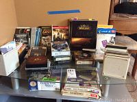 Wide view of table with multiple computer software boxes, CD cases, books including Warcraft Atlas, Avery labels, Family Tree Maker.