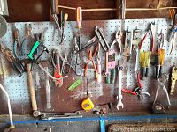 Hand tools hanging on pegboard including pliers, screwdrivers, pipe cutter and wrenches