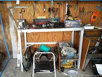 Photo of metal shelf with power drills, toolbox, hand tools, and metal crate below