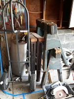 Photo showing two used wooden saw horses, air tire hand truck, and parts of a manual push mower with circular saw blade visible on floor.