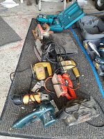 Tools arranged on carpet, showing multiple power tools with cords, including black and orange tools and a teal cordless drill