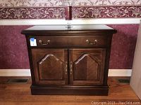 Thomasville sideboard with two doors and one drawer, dark wood finish, brass handles, standing on hardwood floor against patterned wallpaper.