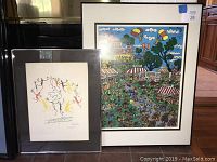 Two framed modern wall art prints by Bruce Brice and Pintauro leaning against a black surface and floor, showing colorful festival scenes.
