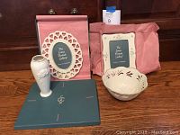 Four collectible Lenox porcelain items on a wooden floor including two picture frames, a bowl, and a vase.