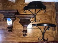 Photo of four wall sconces, two wood and two metal, laid on a wooden floor for display.