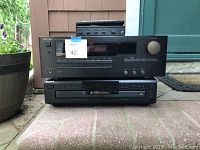 Stacked Sony 5 CD changer at bottom and two Rotel stereo equipment units on top, placed outdoors on tiled ground near a door and plant pot