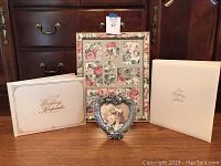 Four wedding themed items on wooden surface: two wedding albums, one floral multi-photo picture frame, and one heart-shaped photo holder with vintage photo.