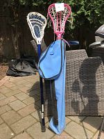Photo showing two lacrosse sticks (boys 31-inch with white and blue head, girls 33-inch with pink head) and a blue carrying case.