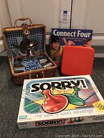 Wicker picnic basket with cutlery, Sorry!, Connect Four, and Travel Monopoly games shown in their boxes/cases.