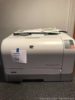 Front view of HP CP1215 LaserJet color printer with power cord and manual placed on top.