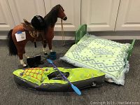 Photo of the American Girl doll accessories including horse with saddle and helmet, boots, bucket, inflatable canoe with paddle, and doll bed with pillow and blanket.